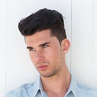 Chico apoyado en pared con corte de pelo moderno.