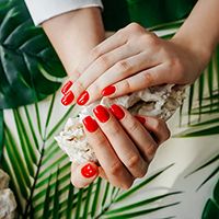 Manos con los uñas pintadas de rojo y con una piedra blanca entre las manos.