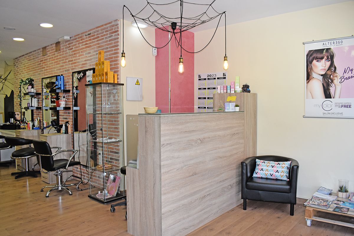 Interior de la peluquería de Sole Solo donde se ve un sillón de la zona de espera con un cojín con dibujos geométricos, el mostrador de la peluquería y los tocadores y al final está la zona infantil.