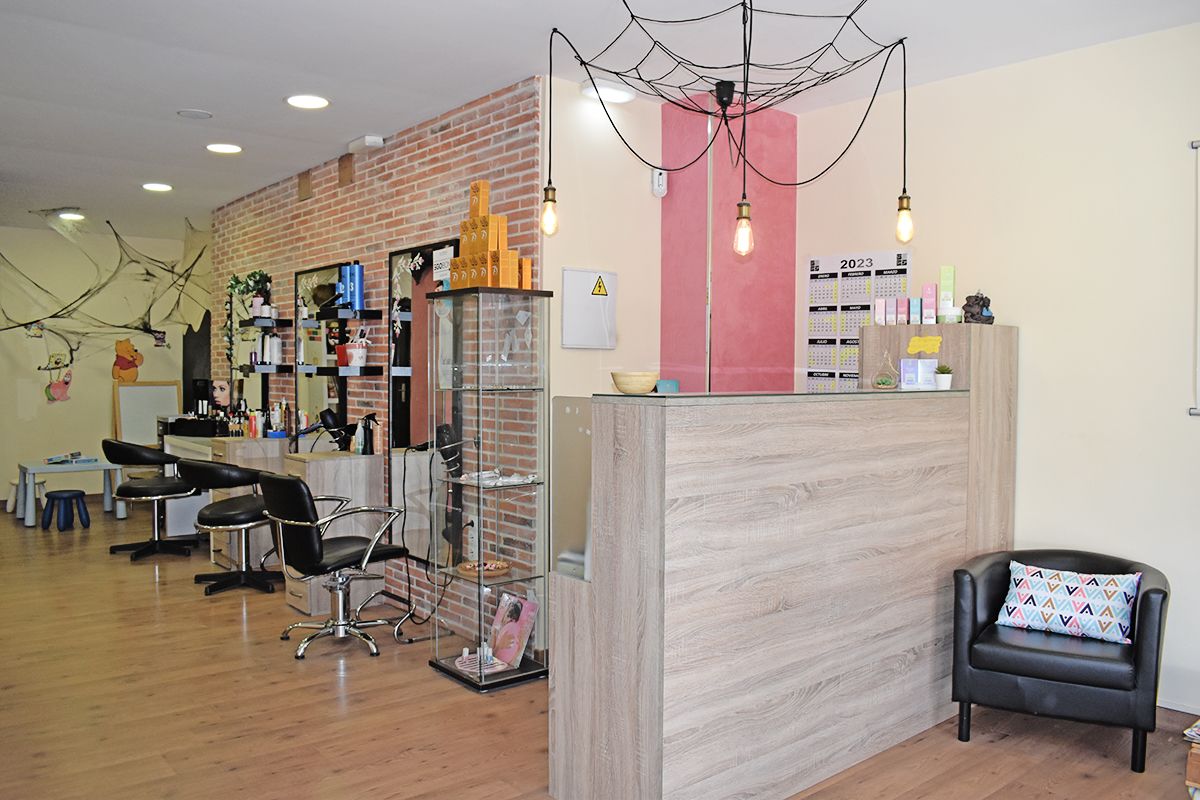 Interior de la peluquería de Sole Solo donde se ve un sillón de la zona de espera con un cojín con dibujos geométricos, el mostrador de la peluquería y los tocadores y al final está la zona infantil.