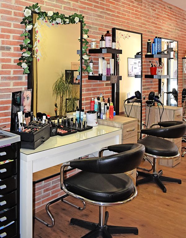 Fotografía de perfil de los tocadores de la peluquería. En el primero se ve todo el producto de maquillaje y en unas baldas de la pared producto de peluquería.